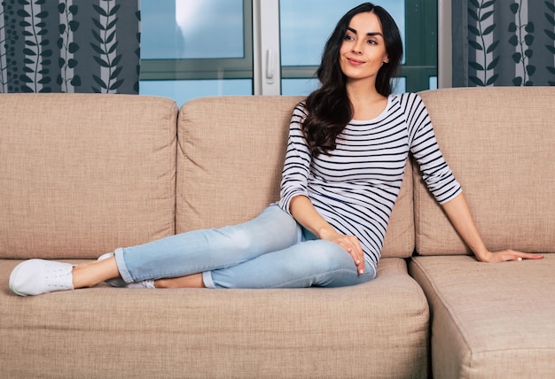 Portrait of a young very beautiful brunette girl sitting on the couch at home