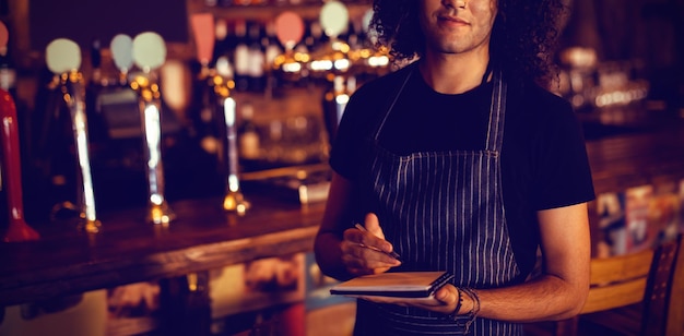 Portrait of young waiter writing on diary