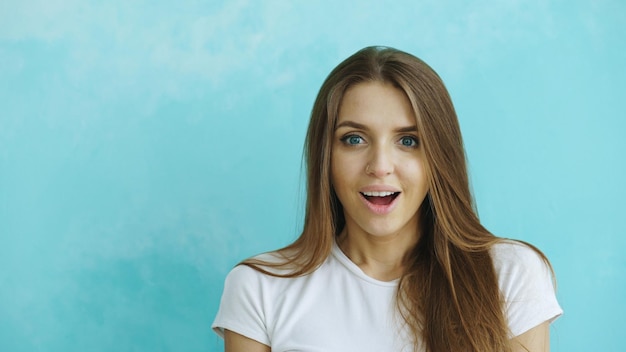 Portrait of young woman actively surprising and wondering looking into camera on blue background