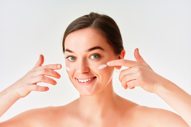 Portrait of young woman applying facial cream for beautiful healthy skin on white background