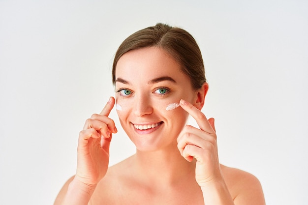 Portrait of young woman applying facial cream for beautiful healthy skin on white background