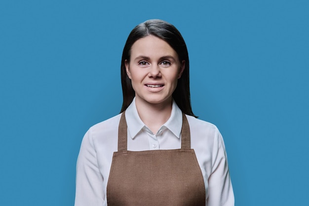 Portrait of young woman in an apron on blue background