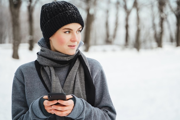 雪に覆われた都市公園で彼女の冬のトレーニング中にスマートフォンを使用して若い女性アスリートの肖像画