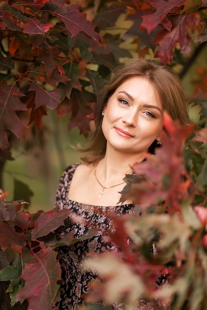 Portrait of a young woman on a background of burgundy leaves in autumn