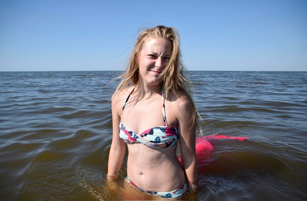 Photo portrait of young woman in bikini standing in sea against sky