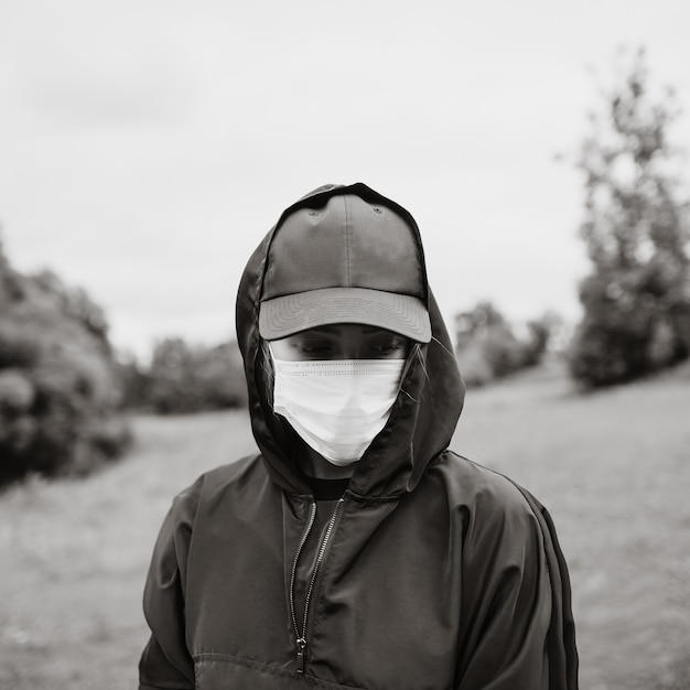 Портрет молодой женщины в черной толстовке с капюшоном и медицинской маске. Черно-белое фото. Настроение грусти, меланхолии, тоски