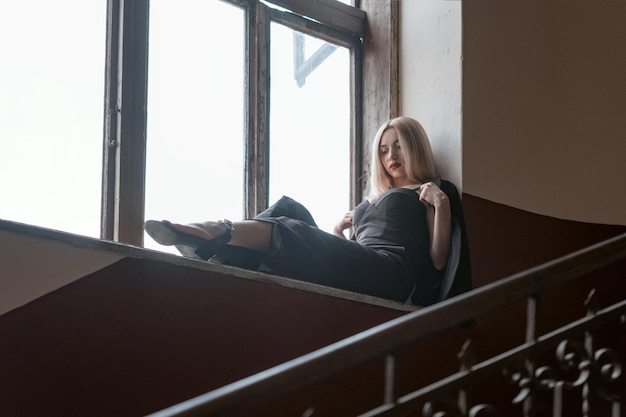 Портрет молодой женщины в черном костюме, сидящей на подоконнике старого здания Одинокая женщина