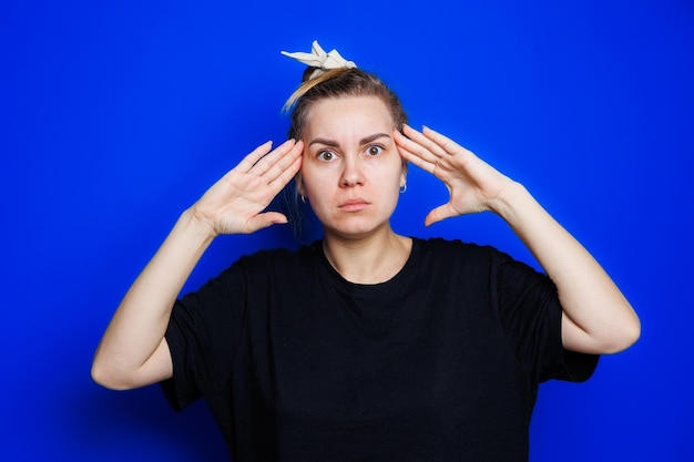 Портрет молодой женщины на синем фоне, держащей голову Головная боль мигрень у женщины