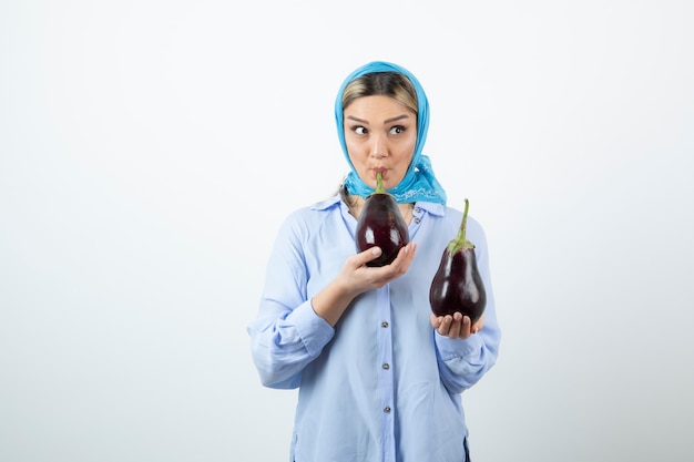 Portrait of young woman in blue shawl holding uncooked eggplants 