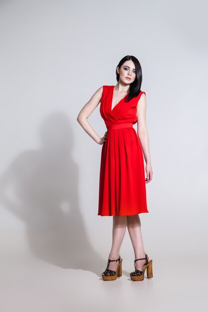 Portrait of young woman in bright red dress looking at camera.Shadow casting on white wall.