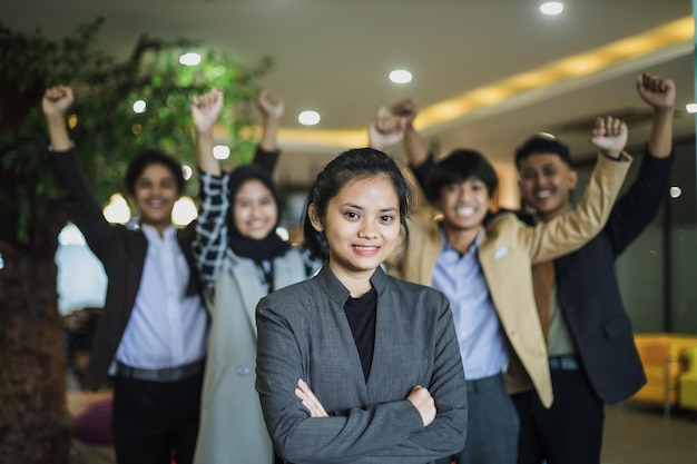 Portrait of young woman in business suit is smiling against motivated coworker background