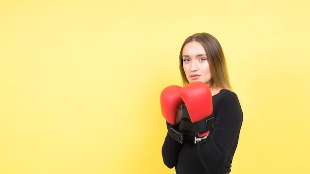 Photo portrait of young woman in casual clothes and hands in boxing gloves against yellow background