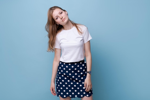 Portrait young woman casual portrait in positive look wide smile beautiful model posing in studio on blue background in casual wear in white t-shirt and polka dot skirt. Caucasian portrait woman