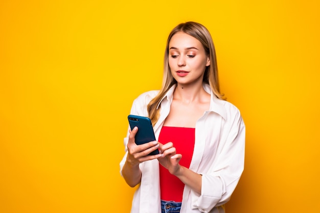 Portrait of young woman chatting by mobile phone isolated over yellow wall wall.