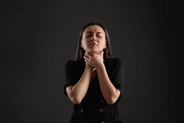 Portrait of young woman choking her neck on black background Personality concept