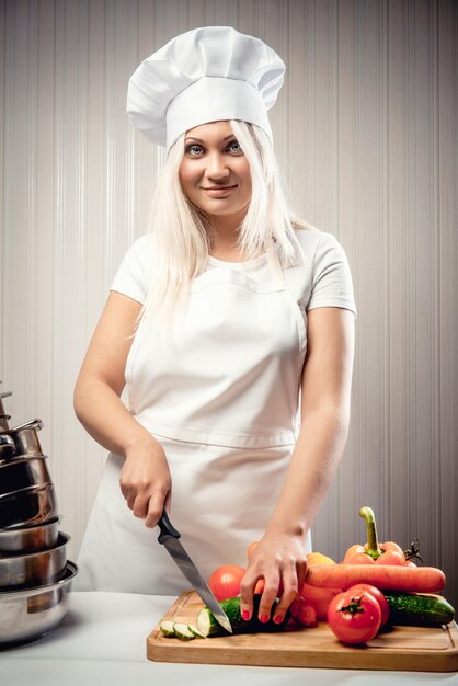 Foto ritratto di una giovane donna che taglia le verdure mentre è in piedi in cucina