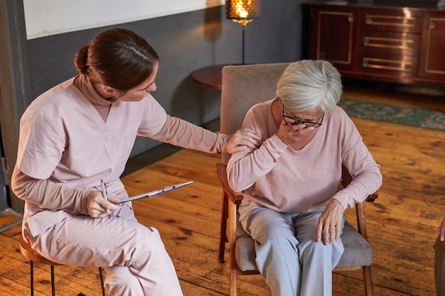 Foto ritratto di giovane donna che conforta la signora anziana che piange durante la sessione di terapia presso la casa di riposo, copia spazio