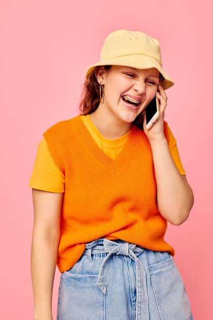 黄色い帽子のファッションで電話でコミュニケーションをとる若い女性の肖像画カットされたビューは変更されていません