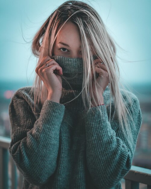 Portrait of young woman covering face with sweater