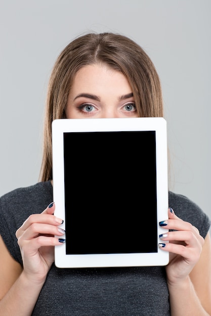 Foto ritratto di una giovane donna che si copre il viso con uno schermo di computer tablet vuoto isolato su uno sfondo bianco