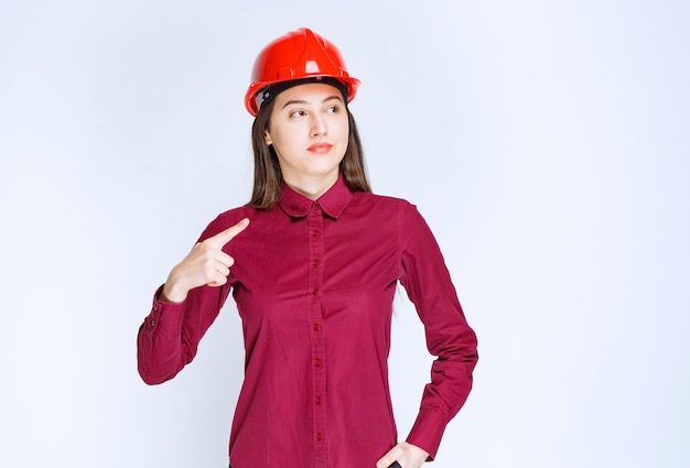 Portrait of young woman in crash helmet pointing aside . 