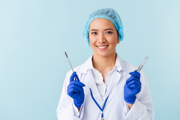 Портрет молодой женщины-врача позирует изолированной над синей стеной, держащей медицинское оборудование.