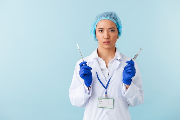 portrait of a young woman doctor posing isolated over blue wall holding medical equipment.