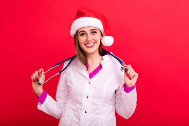 Portrait of a young woman doctor in a white coat with a stethoscope who put on a Santa Claus hat Christmas greetings from doctors