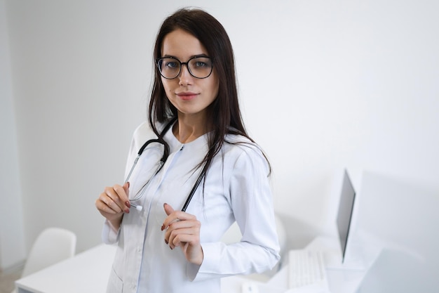 Portrait of young woman doctor with stethoscope standing in office