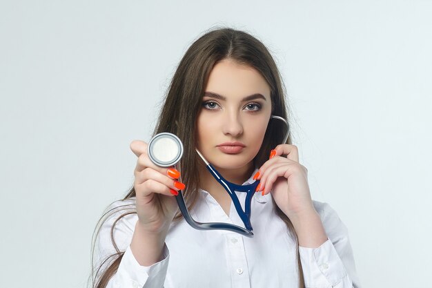 Portrait of a young woman doctor with a stethoscope on a white wall