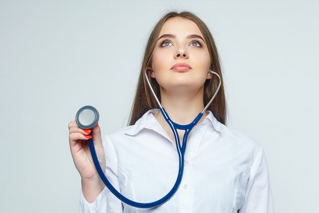 Portrait of a young woman doctor with a stethoscope on a white wall