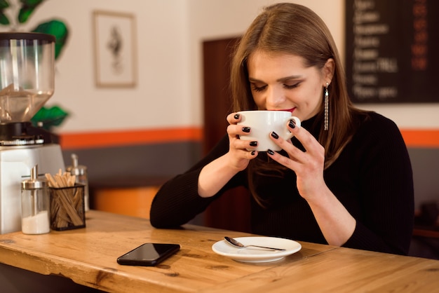 Ritratto di giovane donna che beve il caffè nella caffetteria.