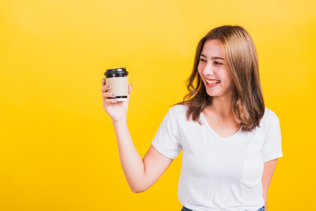 Portrait of young woman drinking glass against yellow background