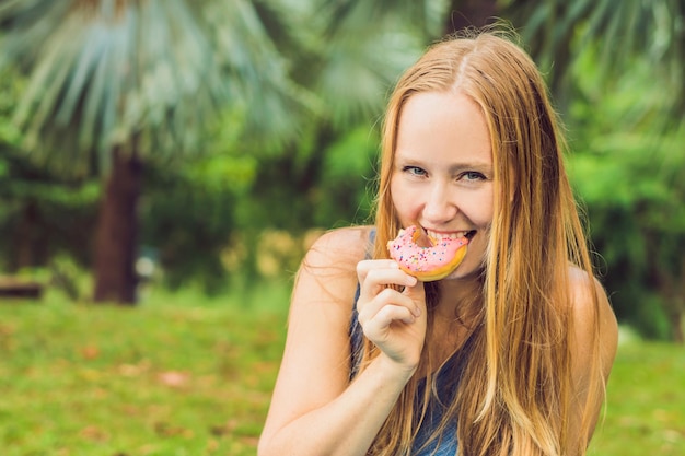 Portrait of a young woman eating a donut against a plant background.