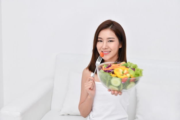 家の壁に横たわってベッドに座ってサラダを食べている若い女性の肖像画