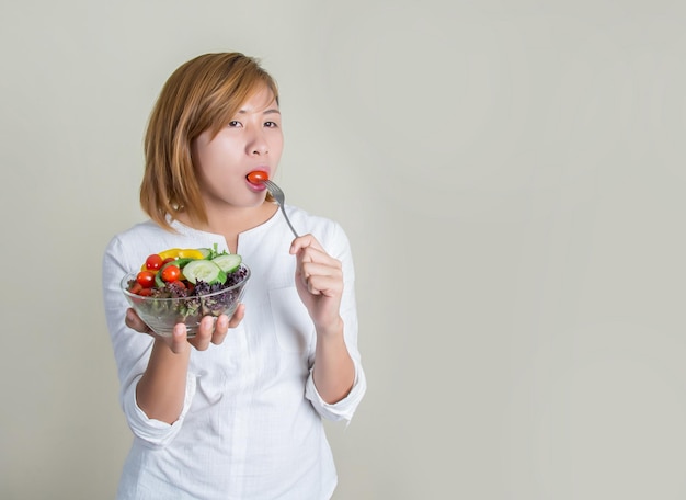 灰色の背景に野菜を食べている若い女性の肖像画