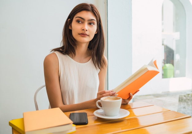 自由な時間を楽しんで、コーヒーショップで屋外に座って本を読んでいる若い女性の肖像画。