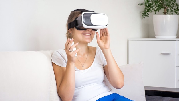 Portrait of young woman enjoying using VR goggles and holding remote control in hand.