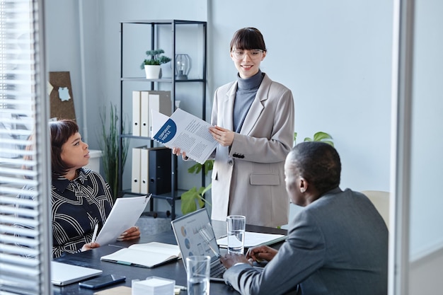 Portrait of young woman executive talking to team in business meeting and holding documents