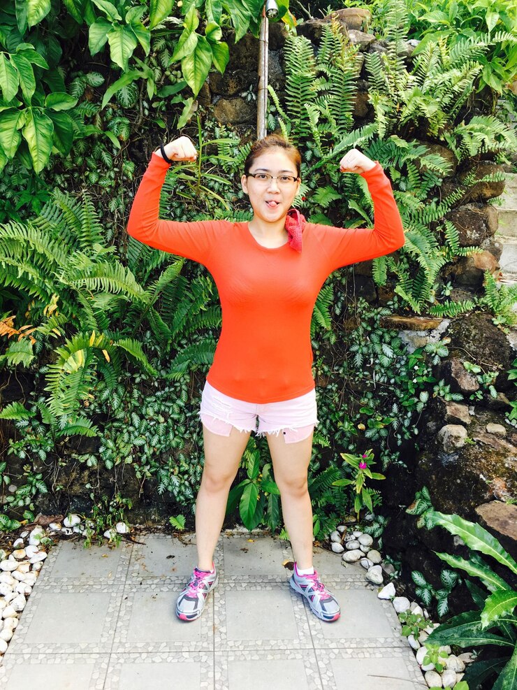 Photo portrait of young woman flexing muscles while standing against plants