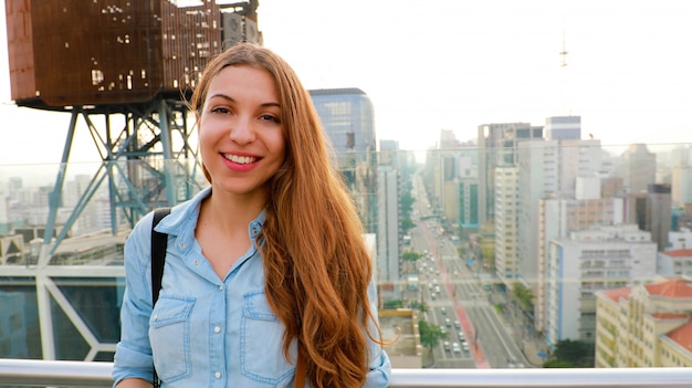 Photo portrait of a young woman in front of the sao paulo skyline with paulista avenue, brazil