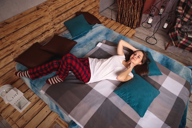 Portrait of a young woman in full-length pajamas lying on a bed, top view.