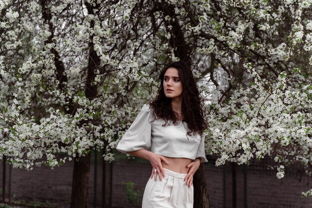 Portrait of young woman in the garden. Attractive girl weared white dress posing near blooming trees.