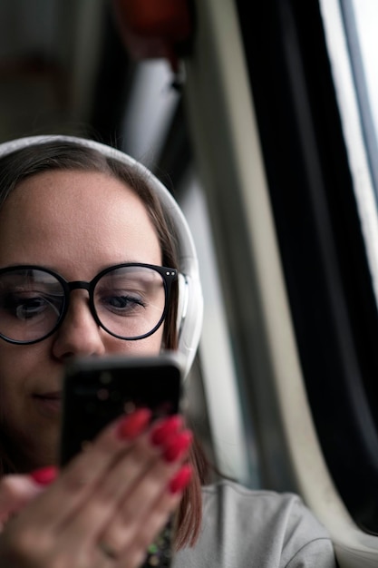 Portrait of young woman in glasses browsing mobile phone riding on train Close up Pretty female using gadget while sitting in suburban train