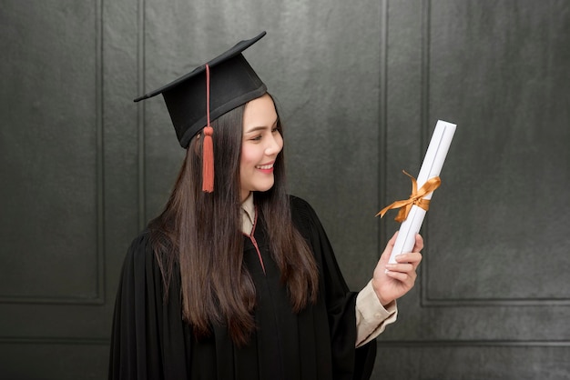 Portrait of young woman in graduation gown smiling and cheering\
on black background