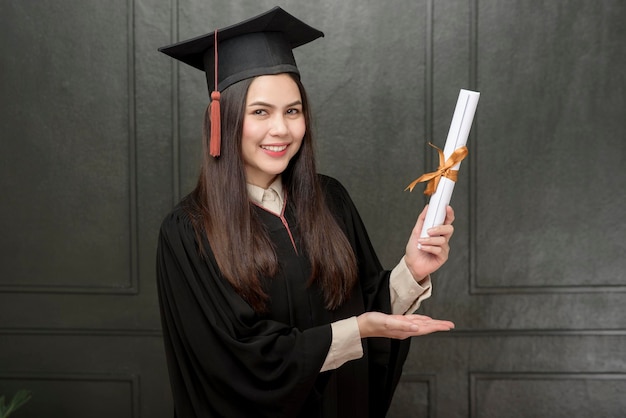 Ritratto di giovane donna in abito di laurea sorridente e tifo su sfondo nero