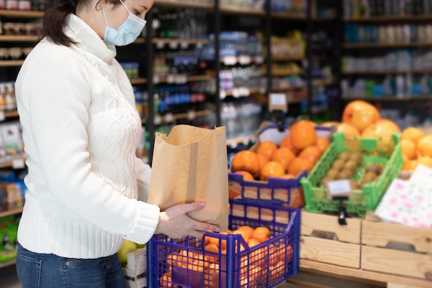 食料品店での若い女性の肖像画保護手袋と医療マスクの店員が彼女の手にコピースペースのある紙袋でポーズをとる