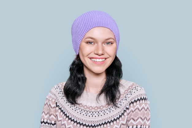 Portrait of young woman in hat in sweater on gray background