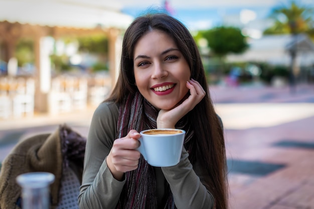 外のカフェに座ってコーヒーを飲んでいる若い女性の肖像画