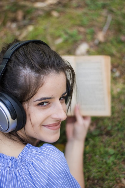 Foto ritratto di una giovane donna che tiene un libro e sorride mentre giace sull'erba